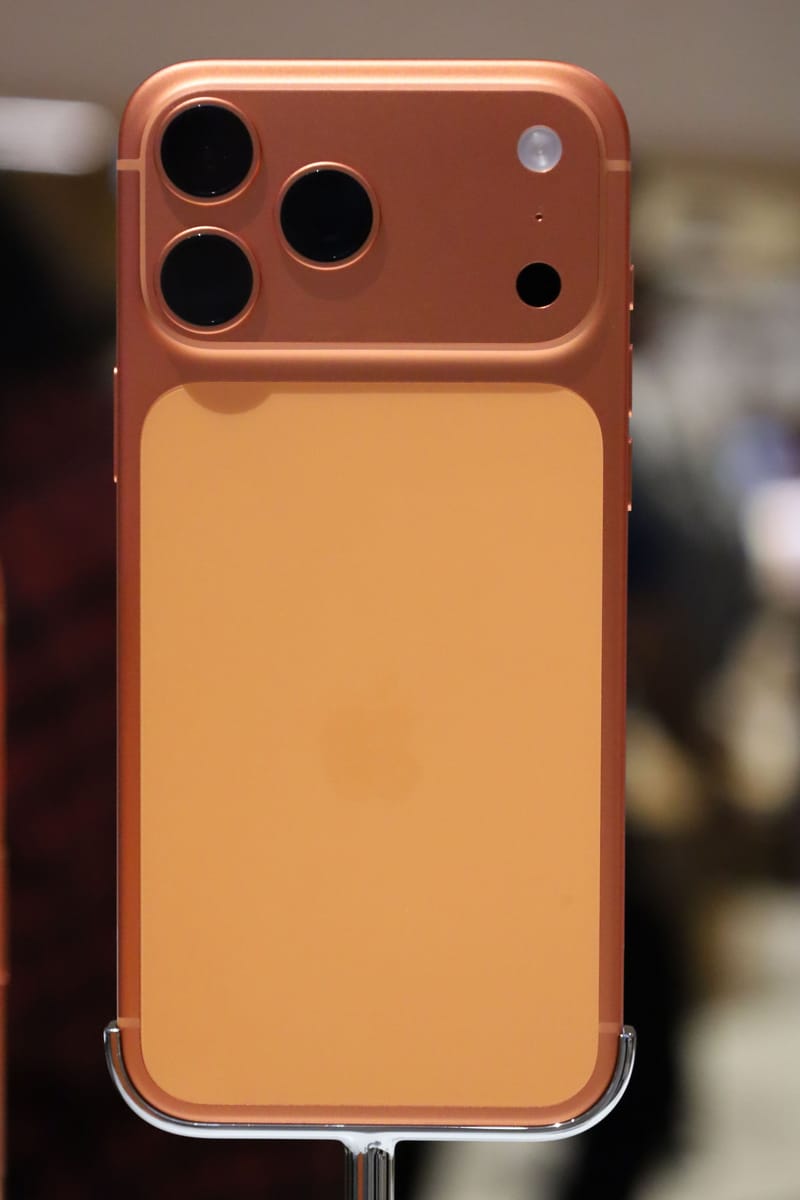 Parte trasera de un iPhone 17 Pro Max en naranja cósmico, con el módulo de tres cámaras, sobre un soporte de exposición