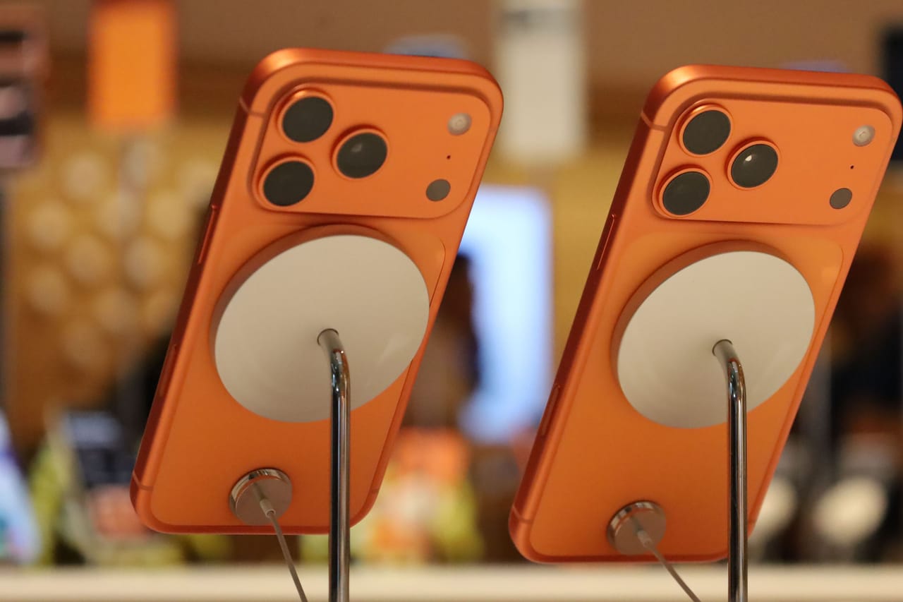 Dos iPhone 17 Pro en naranja cósmico vistos desde atrás, inclinados sobre soportes de exposición